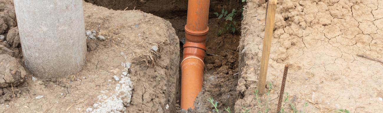 Drainage repairs Surrey. An exposed, orange drain pipe repair.